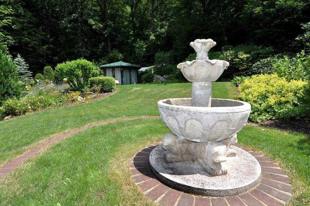 Klassischer Steingartenbrunnen als Blickfang in der weitläufigen, grünen Gartenanlage.