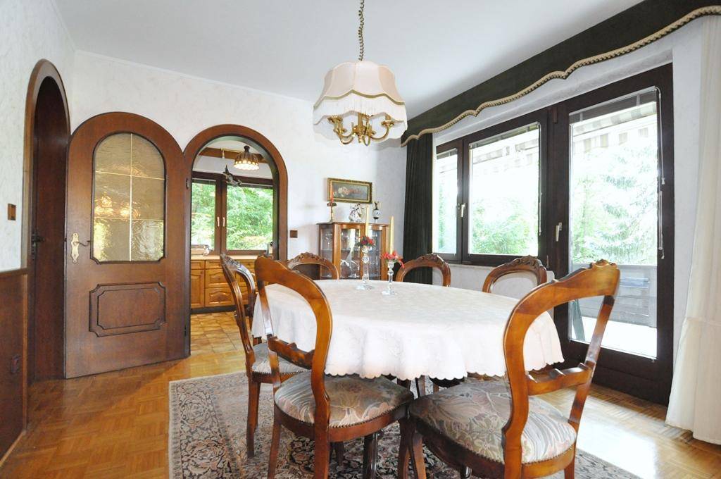 Klassisches Esszimmer mit Holztisch und Stühlen, großen Fenstern und Zugang zu einem Außenbereich.