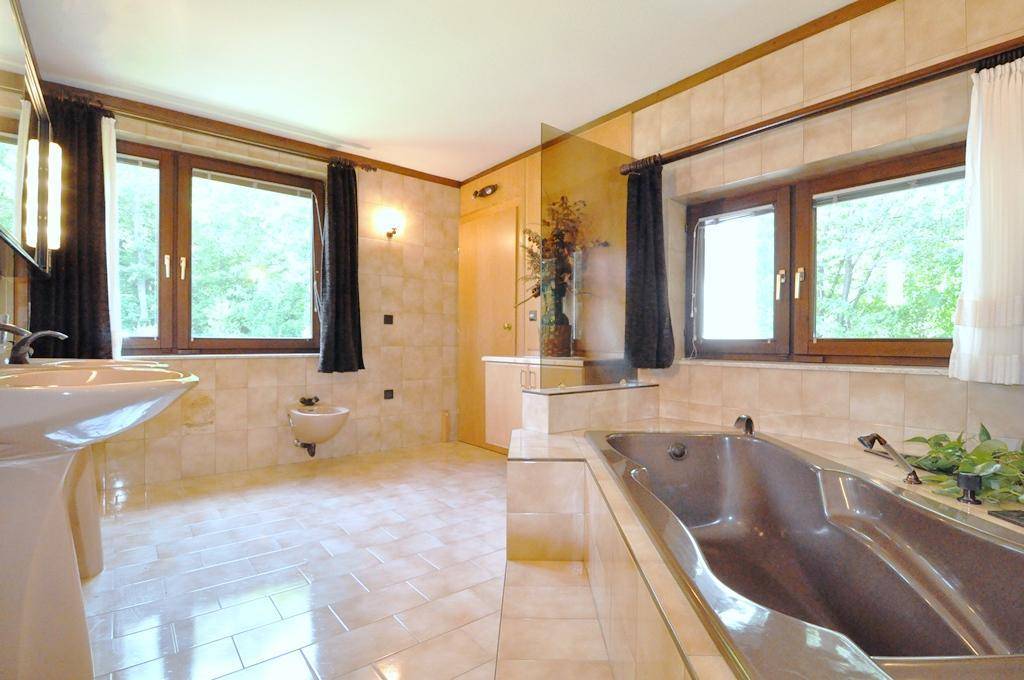 Geräumiges Badezimmer mit großer Badewanne, Doppelwaschbecken und Fenstern mit Blick ins Grüne.