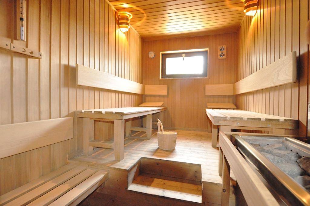 Helle Holzsauna mit Bänken, Saunaofen und kleinem Fenster für Entspannung.