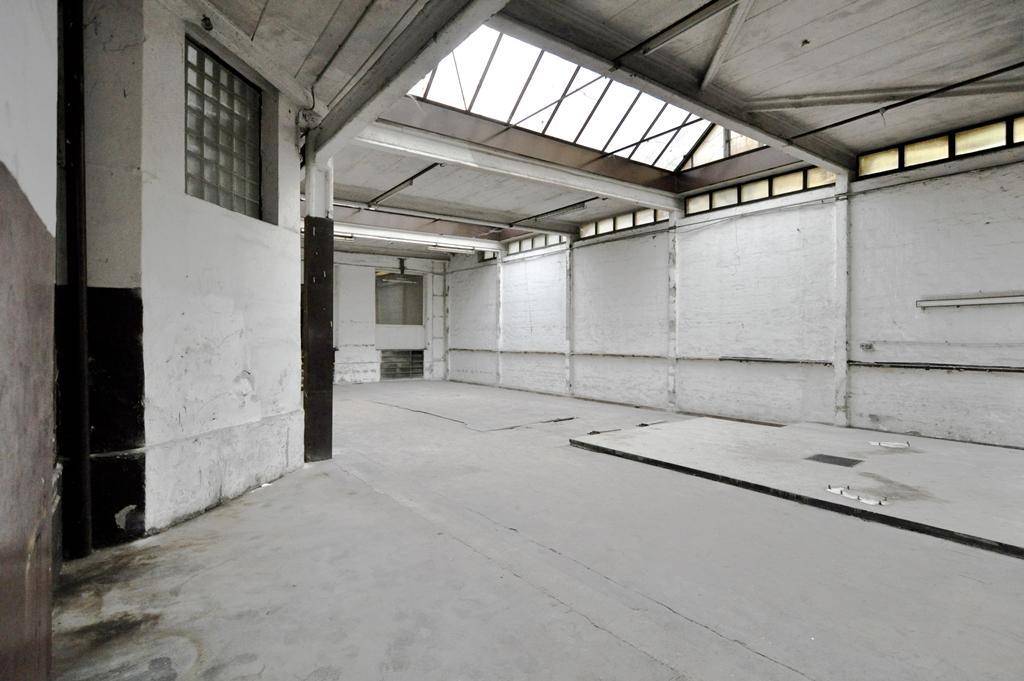 Heller Industrieraum mit Oberlichtern, Betonboden und einer langen Wand, die auf eine vollständige Renovierung wartet.