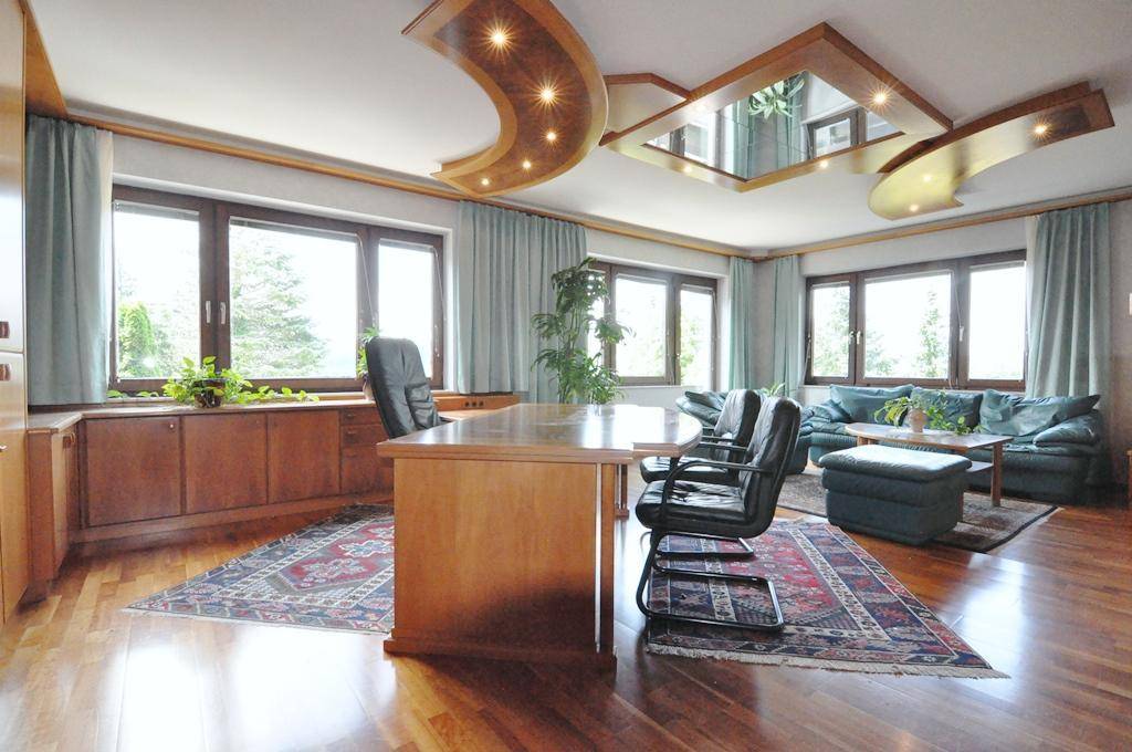 Großzügiges Büro mit Holzboden, stilvoller Deckenkonstruktion und weitem Blick durch die Fensterfront.