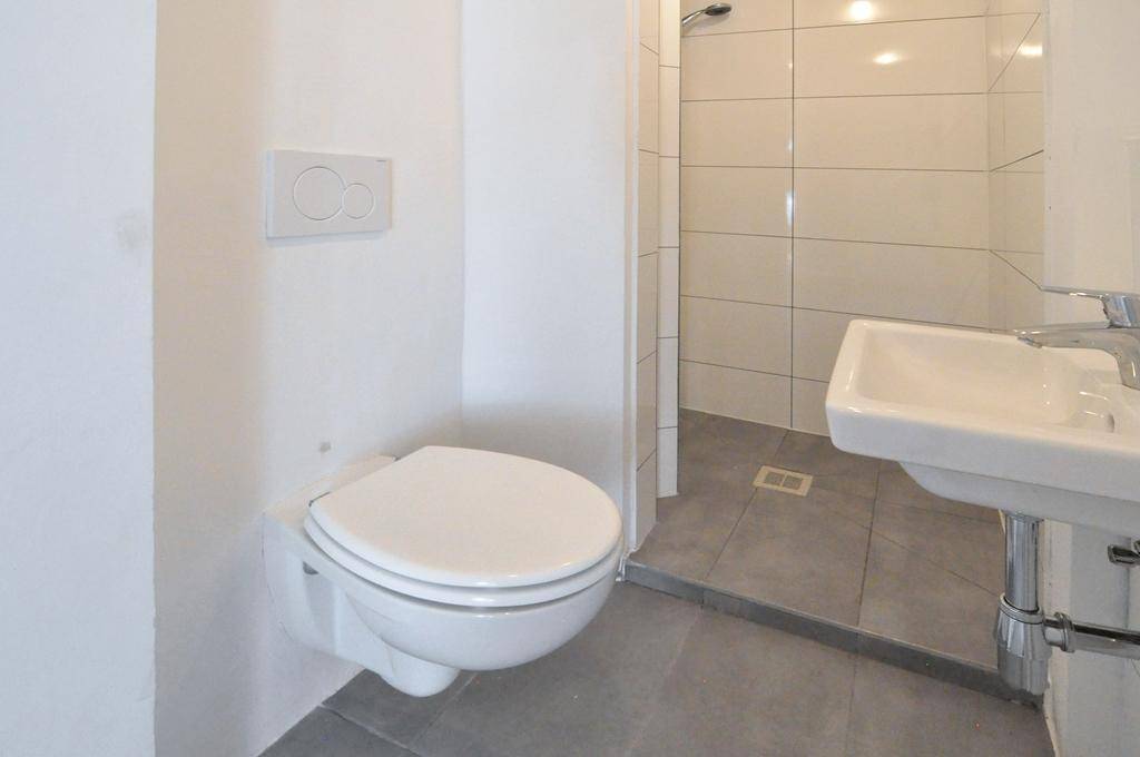 Modernes Badezimmer mit wandhängendem WC, Waschbecken und einer begehbaren Dusche mit Fliesen.