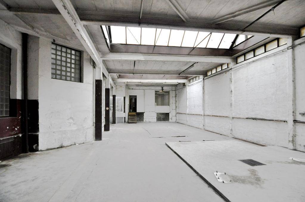Weitläufiger Industrieraum mit Oberlichtern, Betonboden und sichtbaren Trägern, der eine umfassende Modernisierung erfordert.