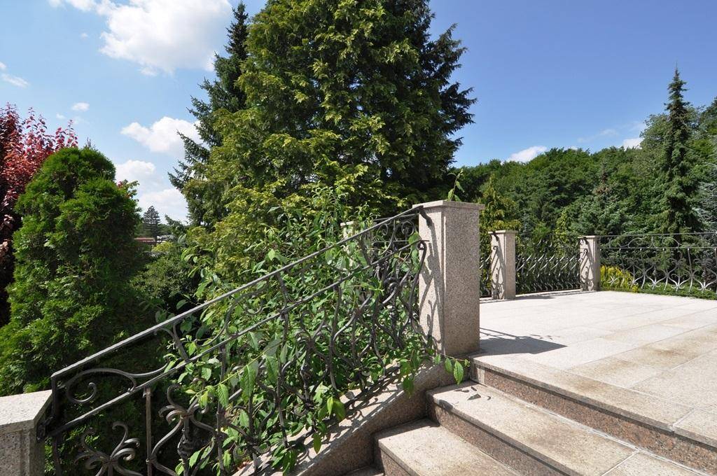 Elegante Steintreppe mit schmiedeeisernem Geländer führt zu einer großzügigen, gepflasterten Terrasse.