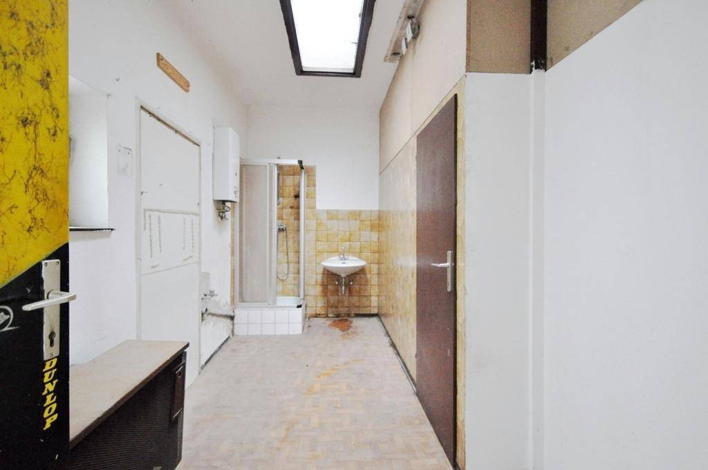 Einfaches Badezimmer mit Duschkabine, Waschbecken und alten Fliesen, das eine vollständige Renovierung benötigt.