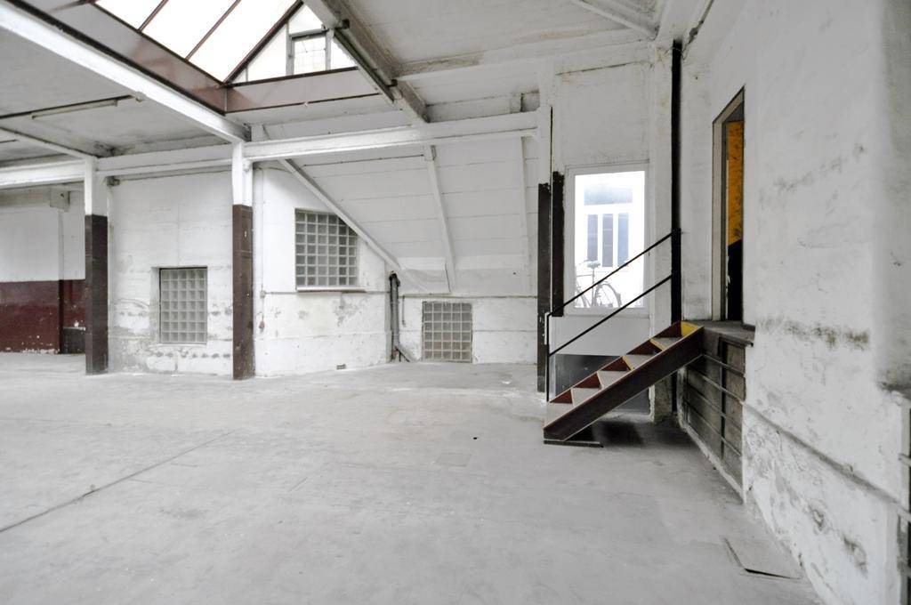Heller Industrieraum mit Oberlichtern, Betonboden und einer kleinen Treppe, die zu einem erhöhten Bereich führt und renovierungsbedürftig ist.
