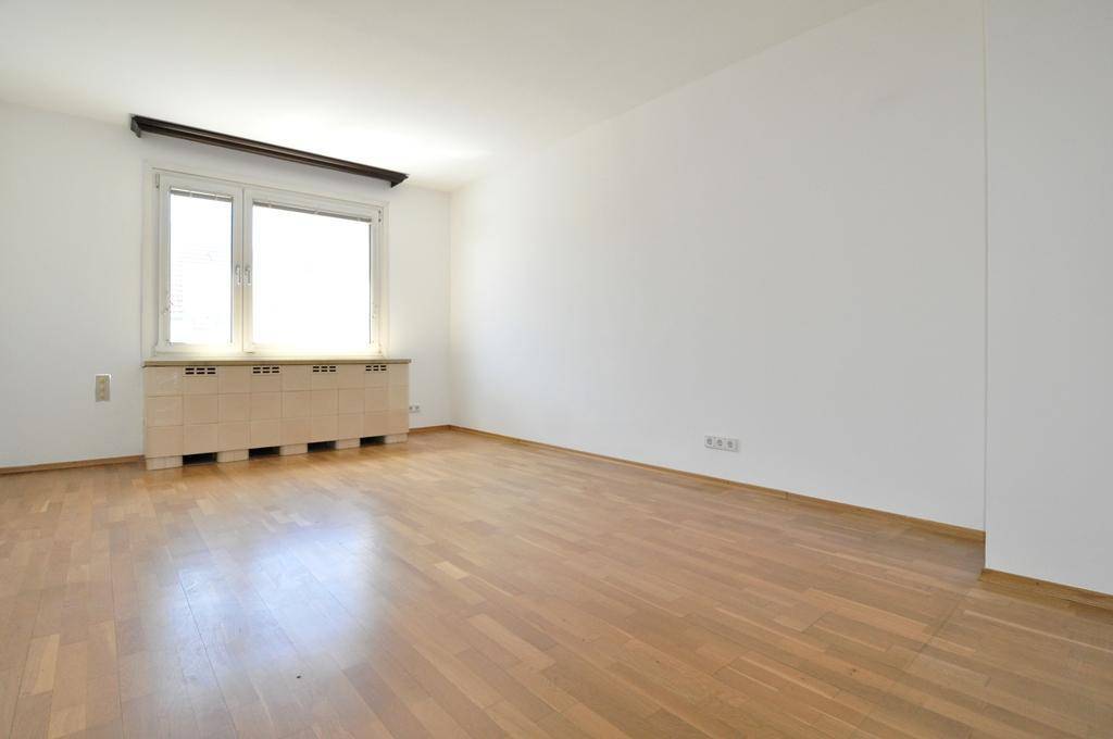 Lichtdurchflutetes Zimmer mit Parkettboden und einem breiten Fensterbereich.