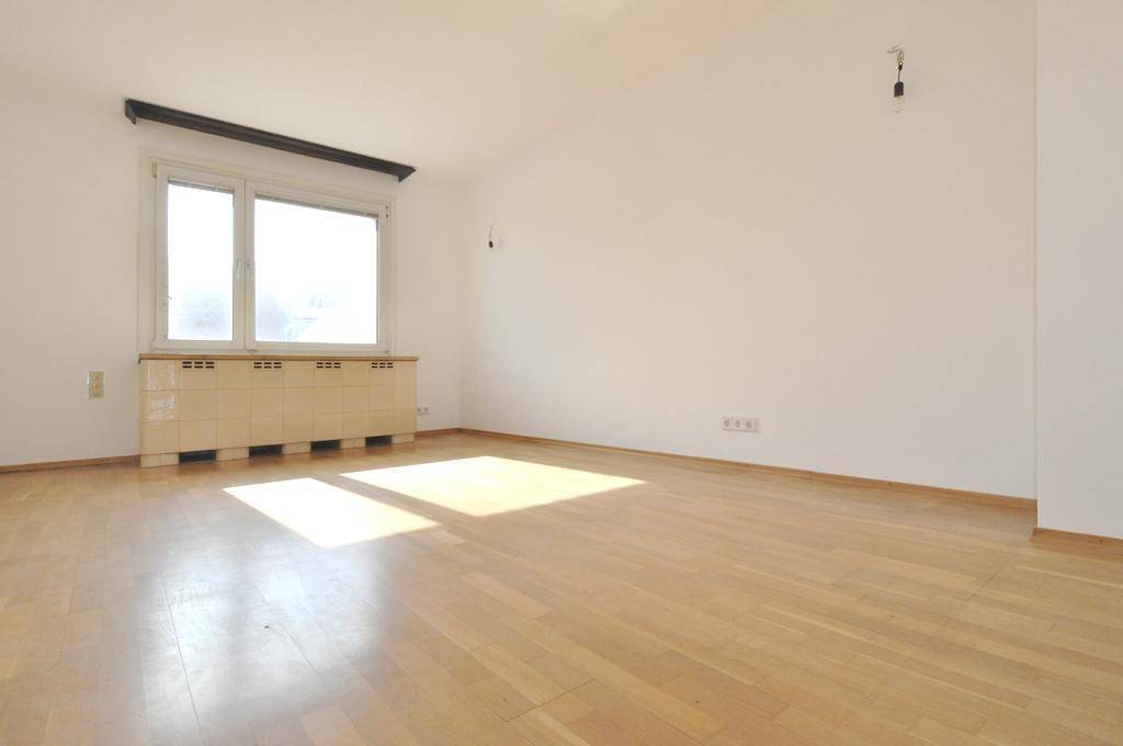 Geräumiges Zimmer mit Parkettboden, weiß gestrichenen Wänden und viel Tageslicht durch das Fenster.