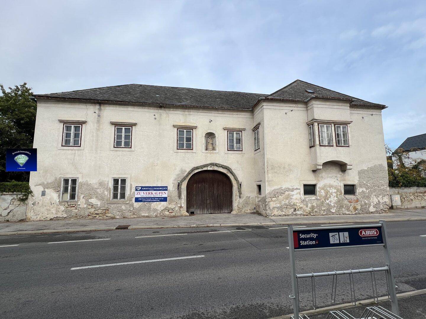 Historisches Gebäude an der Straße mit Torbogen und einem 'ZU VERKAUFEN' Schild.