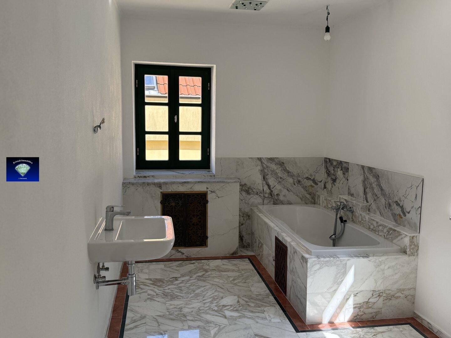 Elegantes Badezimmer mit Marmorfliesen, eingebauter Badewanne und modernem Waschbecken unter einem Fenster.