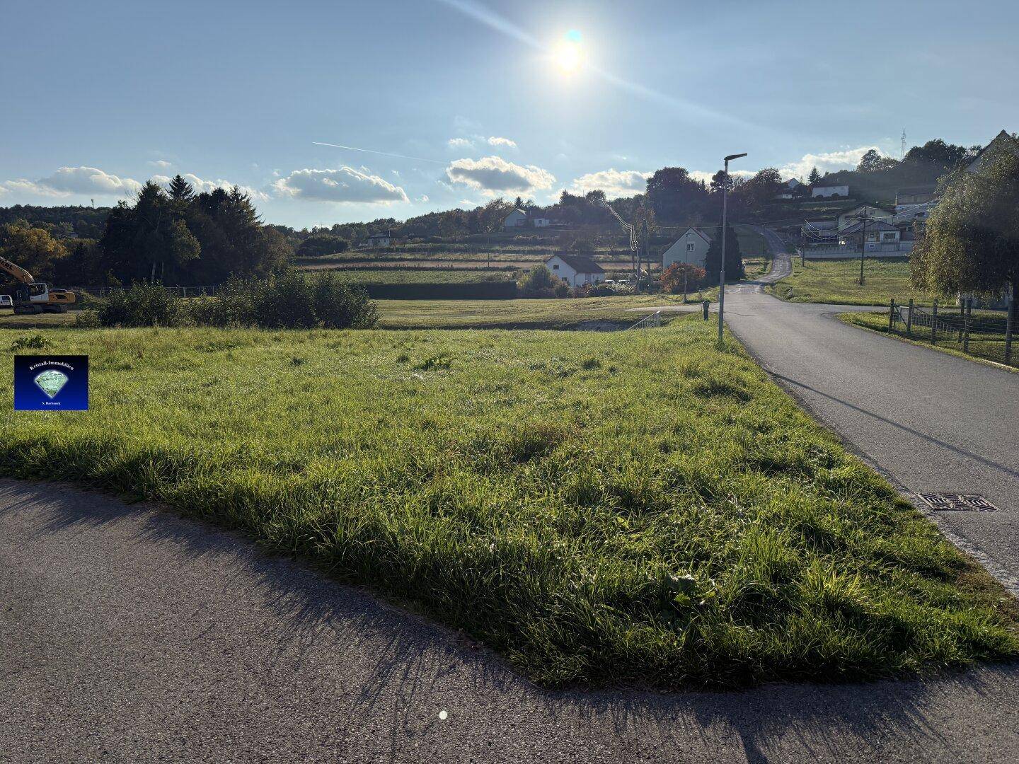 Weitläufiges Grundstück mit grüner Wiese und angrenzender Straße, umgeben von ländlicher Landschaft.