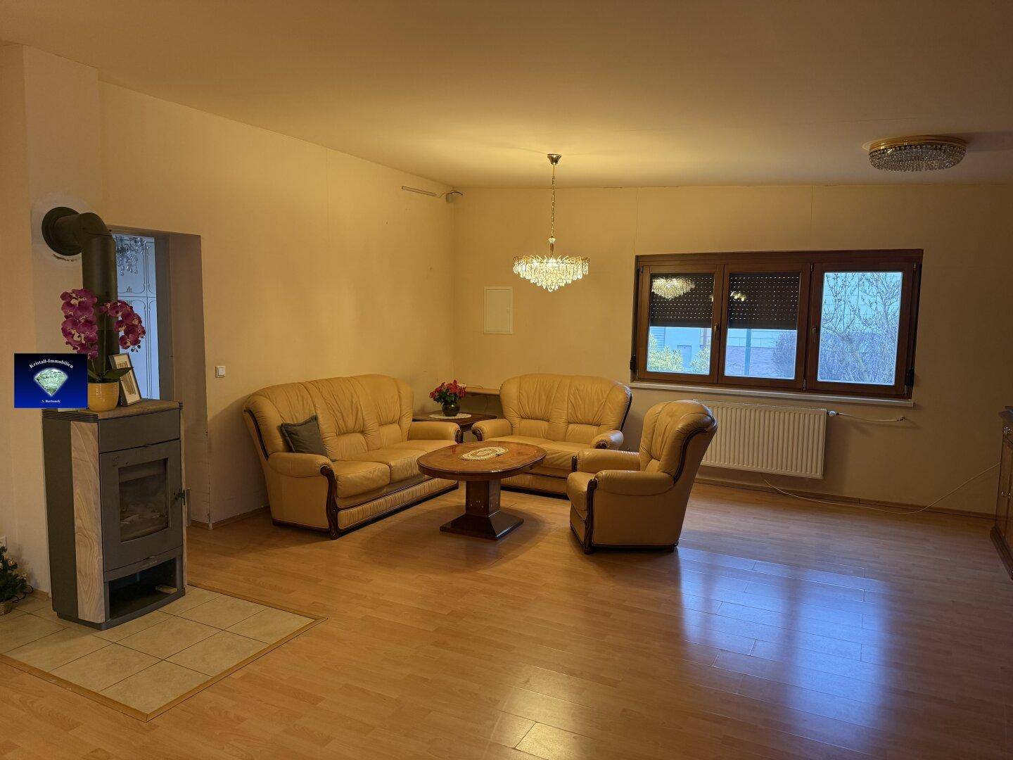 Gemütliches Wohnzimmer mit Kaminofen, hellen Ledersofas und Holzboden.