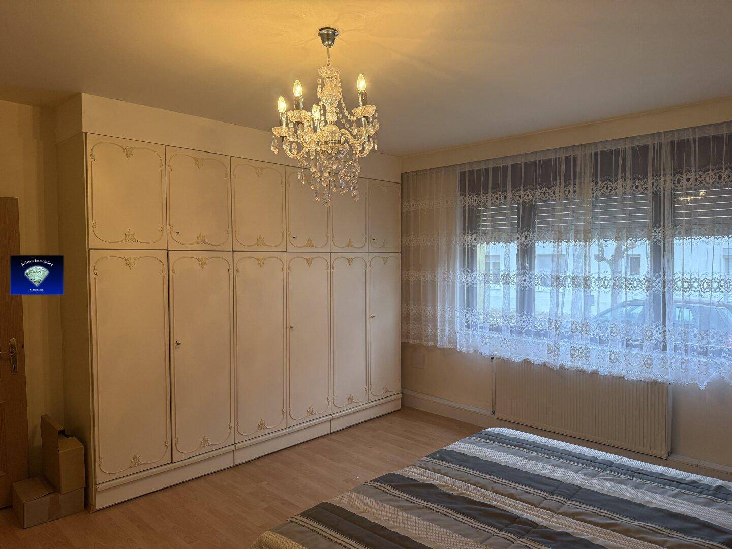 Schlafzimmer mit großem Einbauschrank, Kronleuchter und Blick auf die Straße.