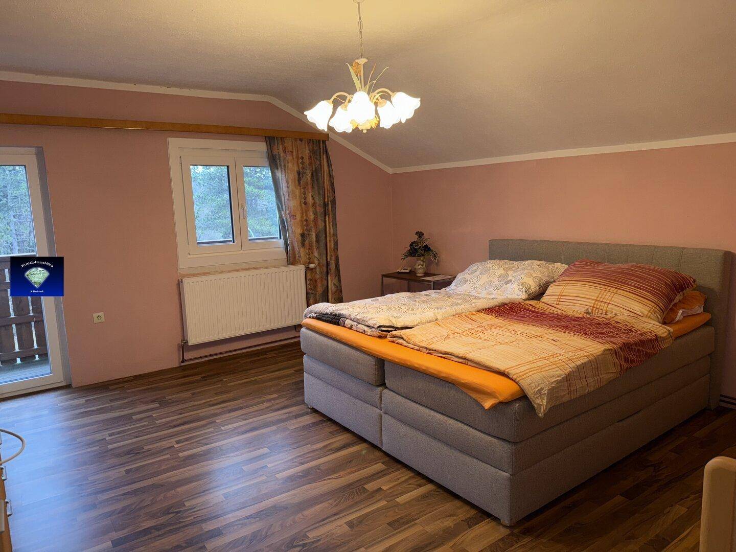 Schlafzimmer mit Holzboden, rosa Wänden und Zugang zu einem kleinen Balkon.