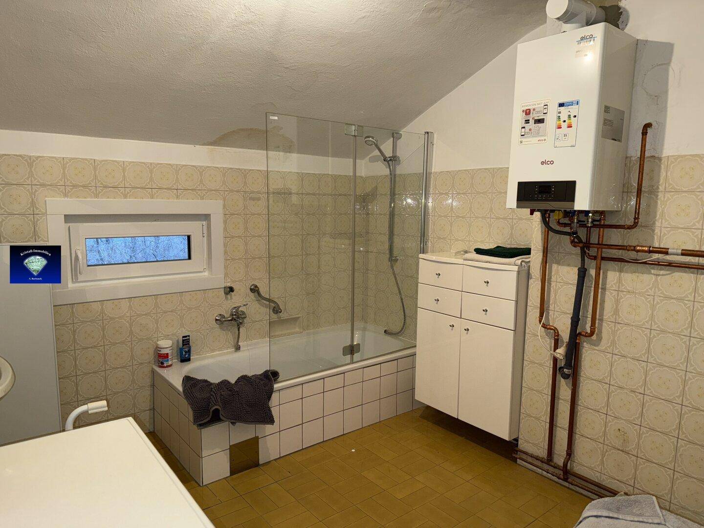Badezimmer mit Badewanne, Duschabtrennung und Gastherme an der Wand.