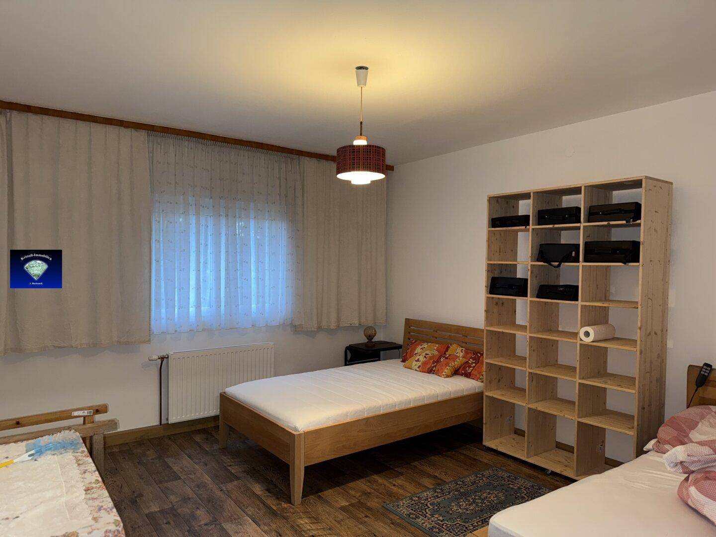 Helles Schlafzimmer mit zwei Einzelbetten, Holzregal und Holzboden.