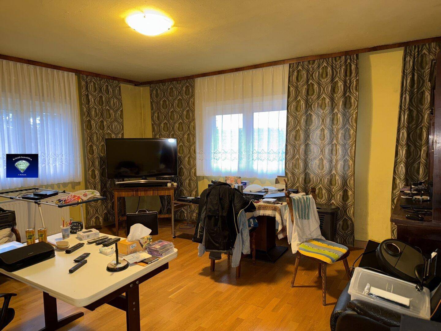 Wohnzimmer mit Parkettboden, mehreren Fenstern und traditionellen Vorhängen.