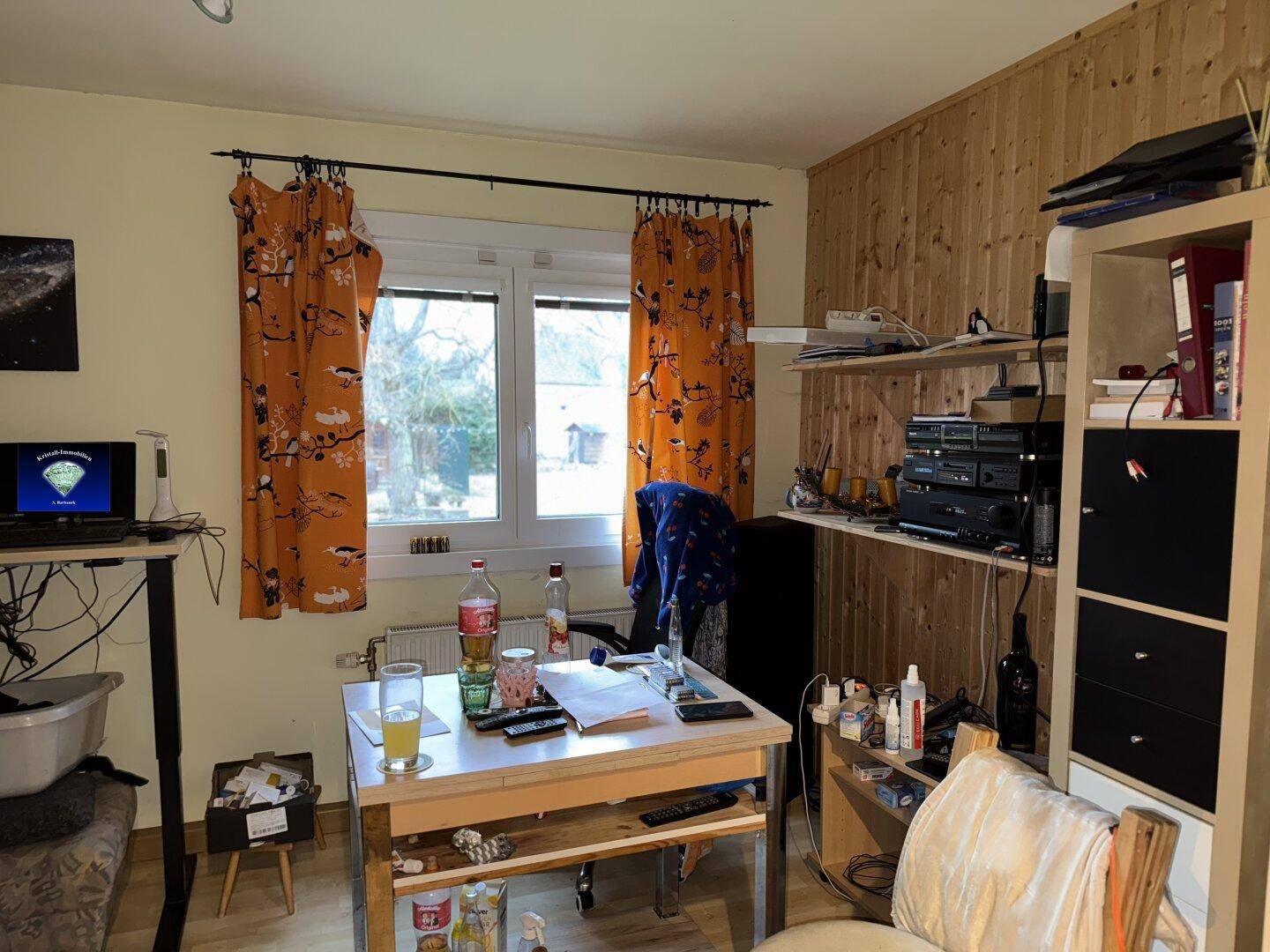 Arbeitszimmer mit Holzvertäfelung, Schreibtisch und orangefarbenen Vorhängen.