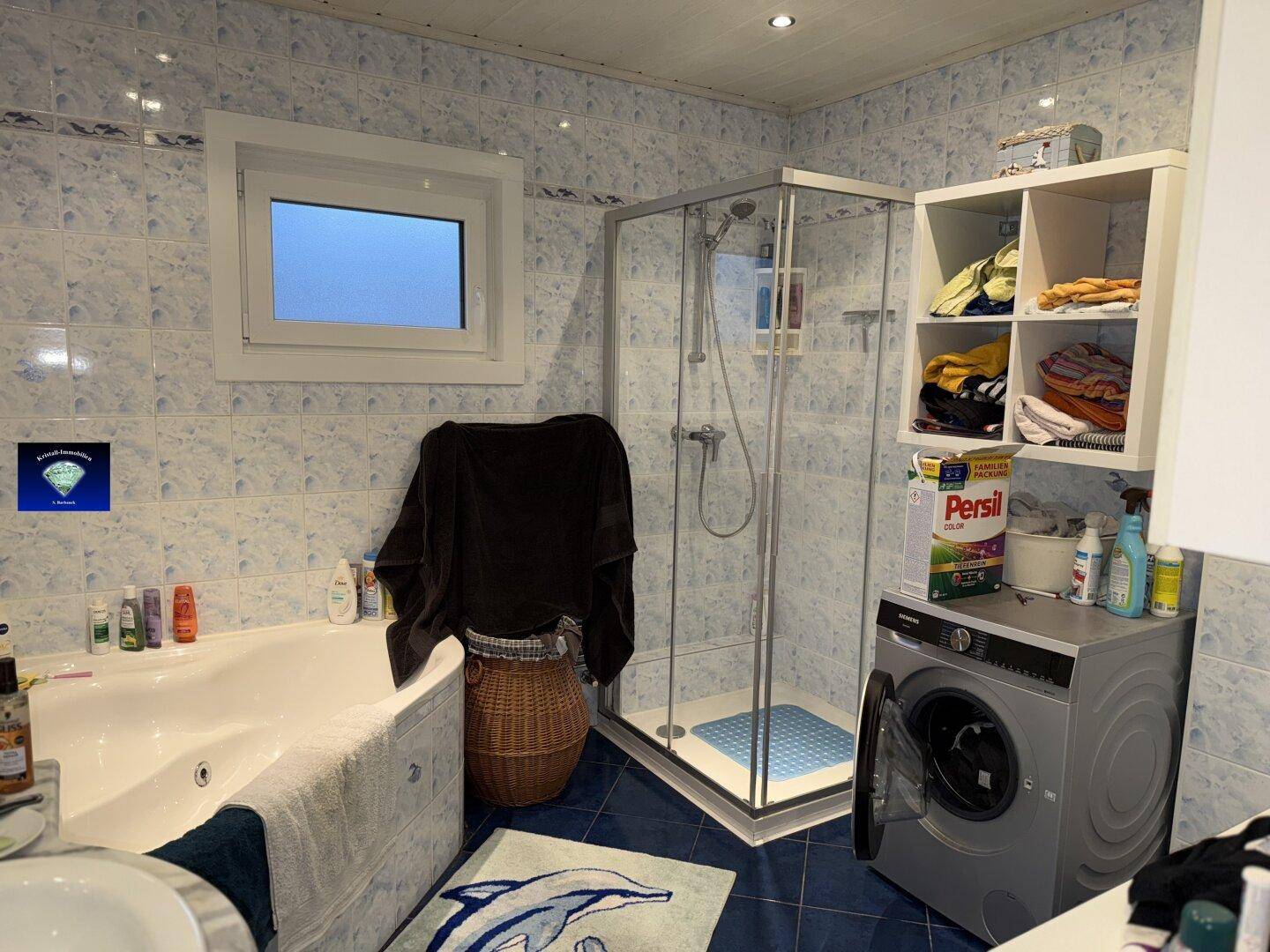 Modernisiertes Badezimmer mit blauen Fliesen, Badewanne, Dusche und Waschmaschine.