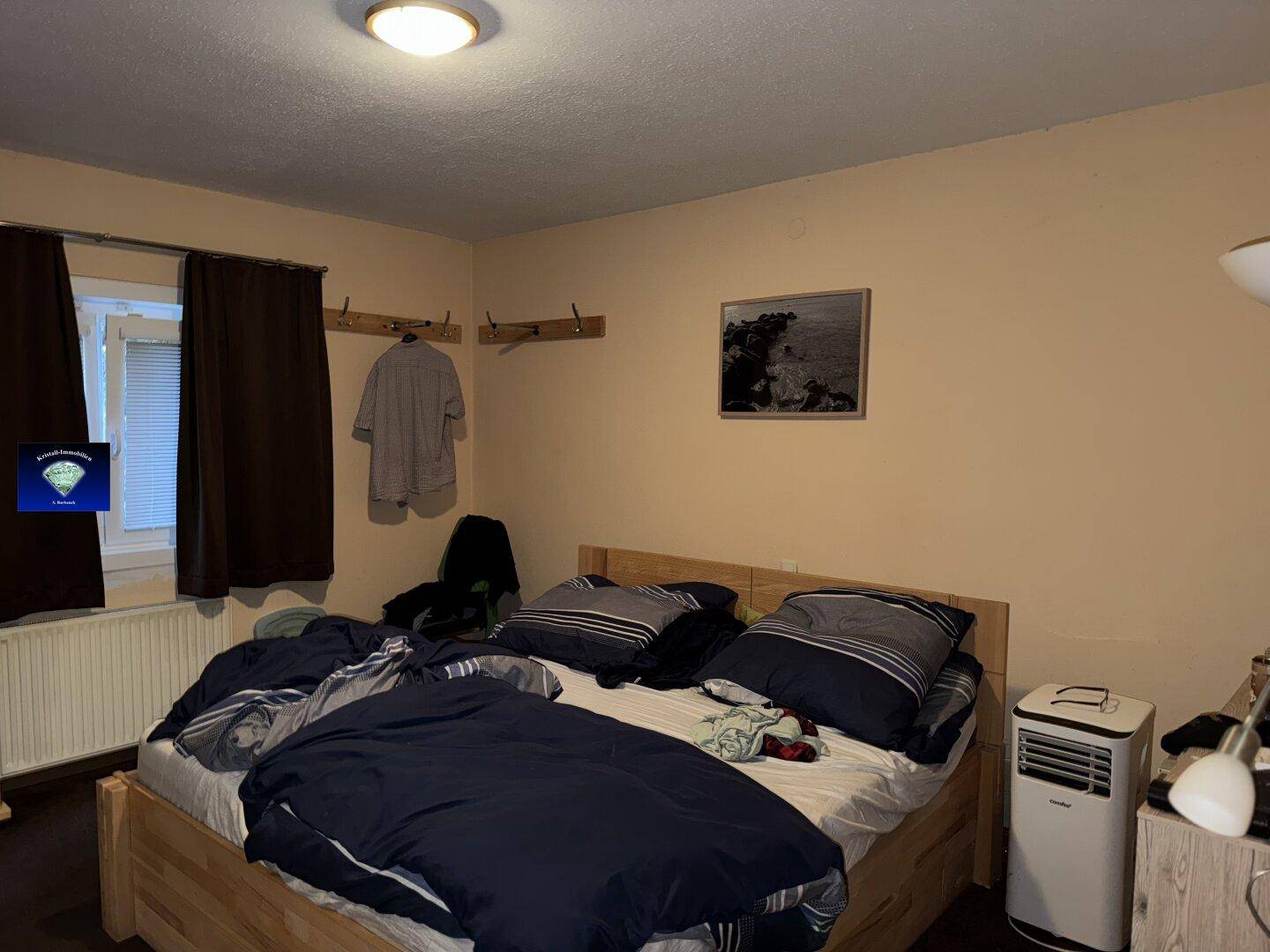 Schlafzimmer mit Doppelbett, beigen Wänden und dunklen Vorhängen.