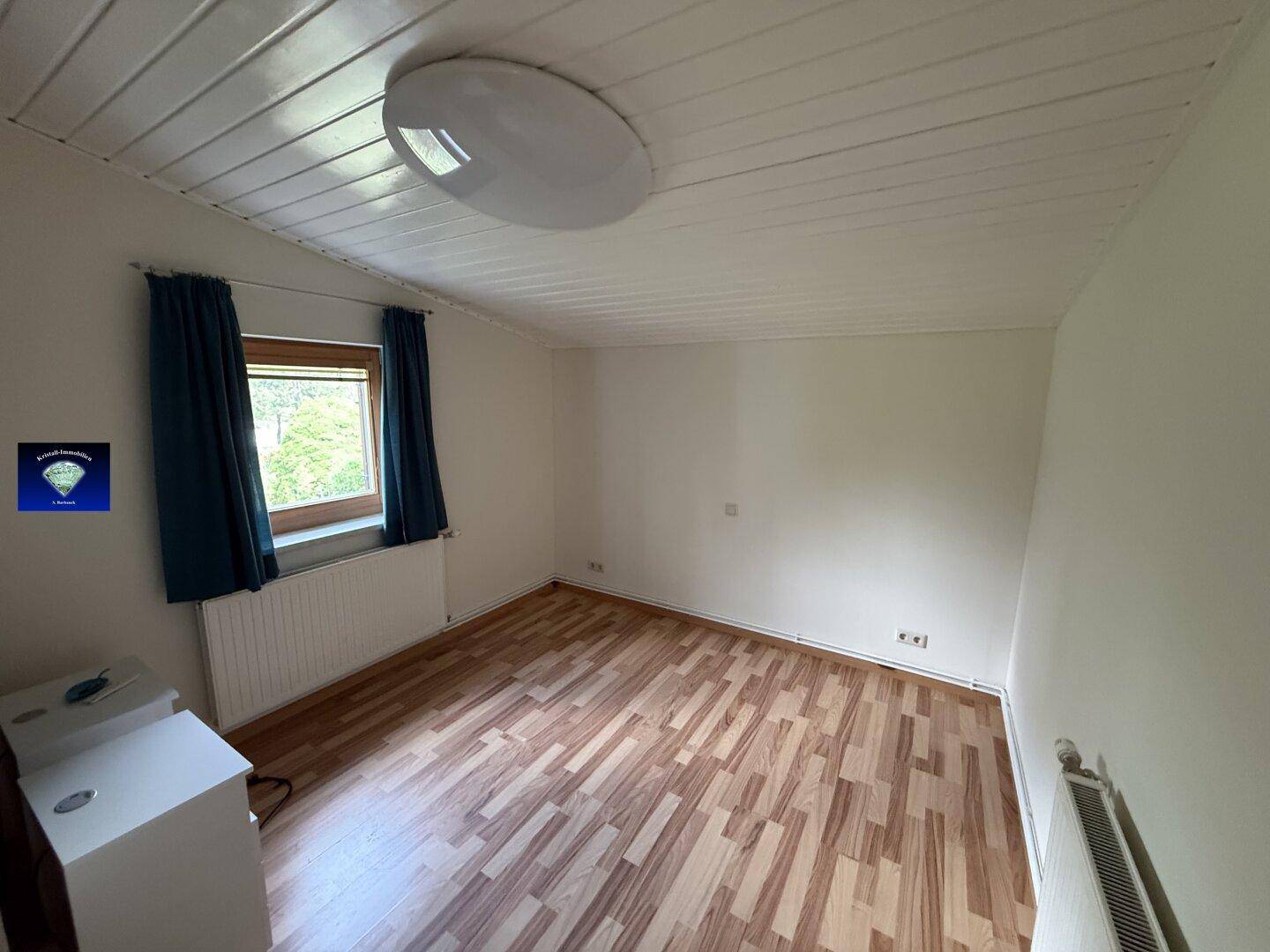 Helles Schlafzimmer mit Laminatboden und einem Fenster, das viel Tageslicht hereinlässt.