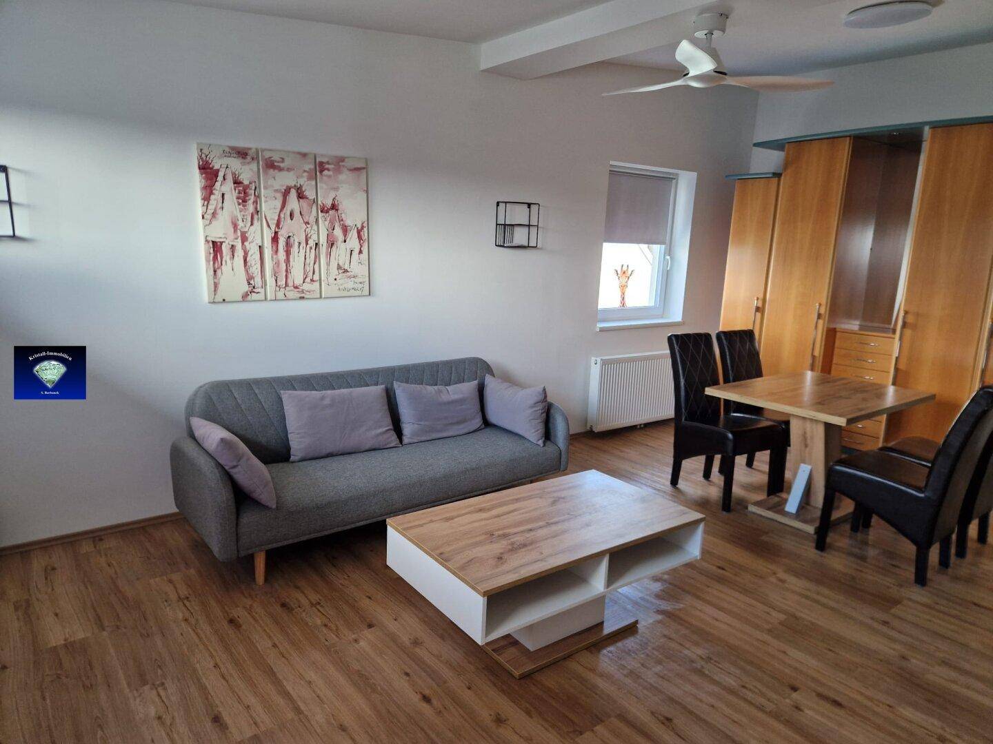 Heller Wohn- und Essbereich mit Holzoptikboden, Sofa, Esstisch und Deckenventilator.