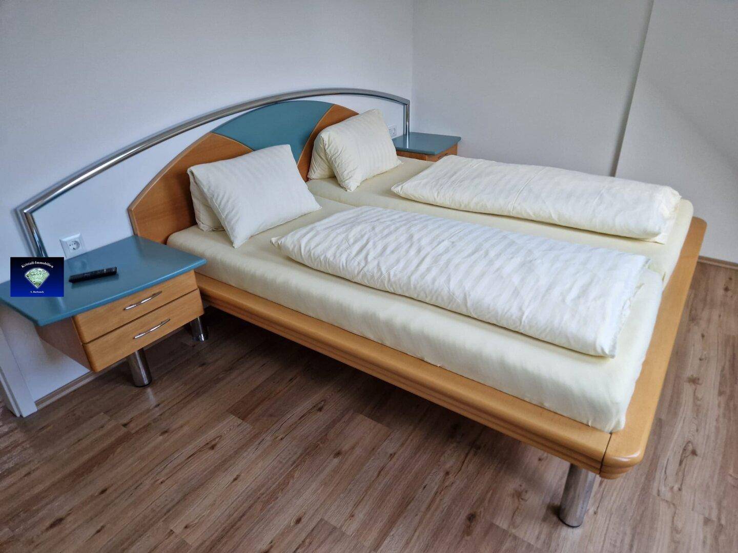 Schlafzimmer mit Doppelbett, Holzoptikboden und Nachttischen in hellem Holzton.