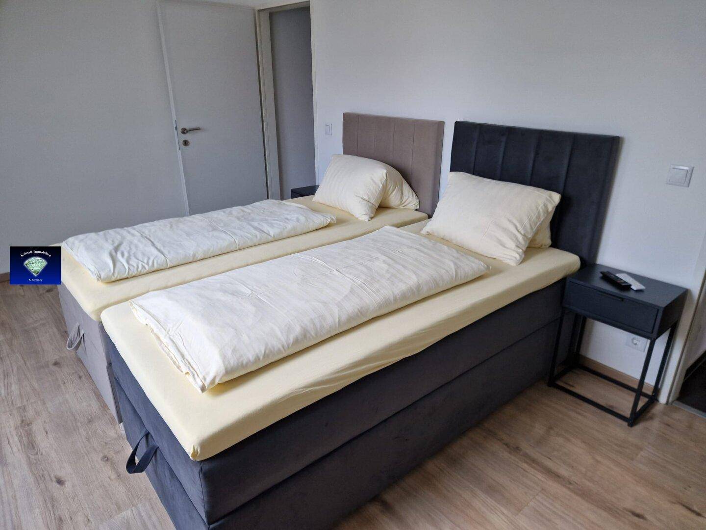 Schlafzimmer mit zwei Einzelbetten, Holzoptikboden und schlichtem, modernem Design.