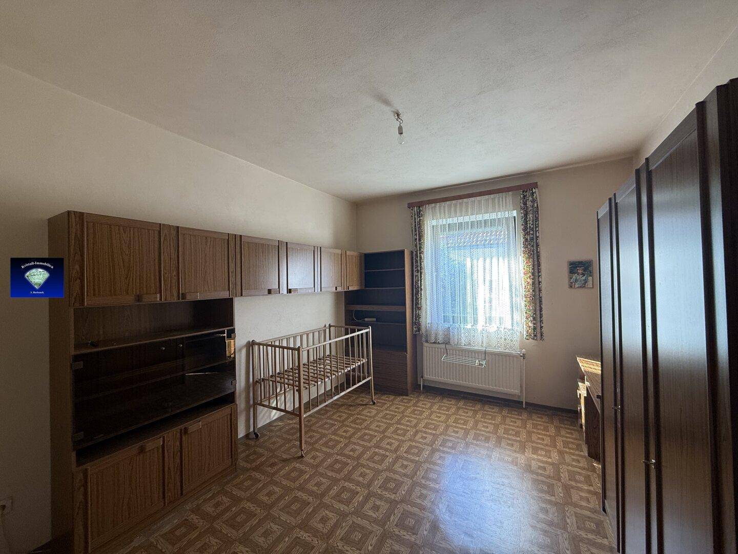 Schlafzimmer mit Kinderbett, Holzschränken und gemustertem Bodenbelag.