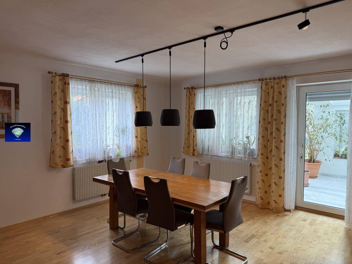 Heller Essbereich mit Holztisch, modernen Pendelleuchten und Zugang zu einem Wintergarten.