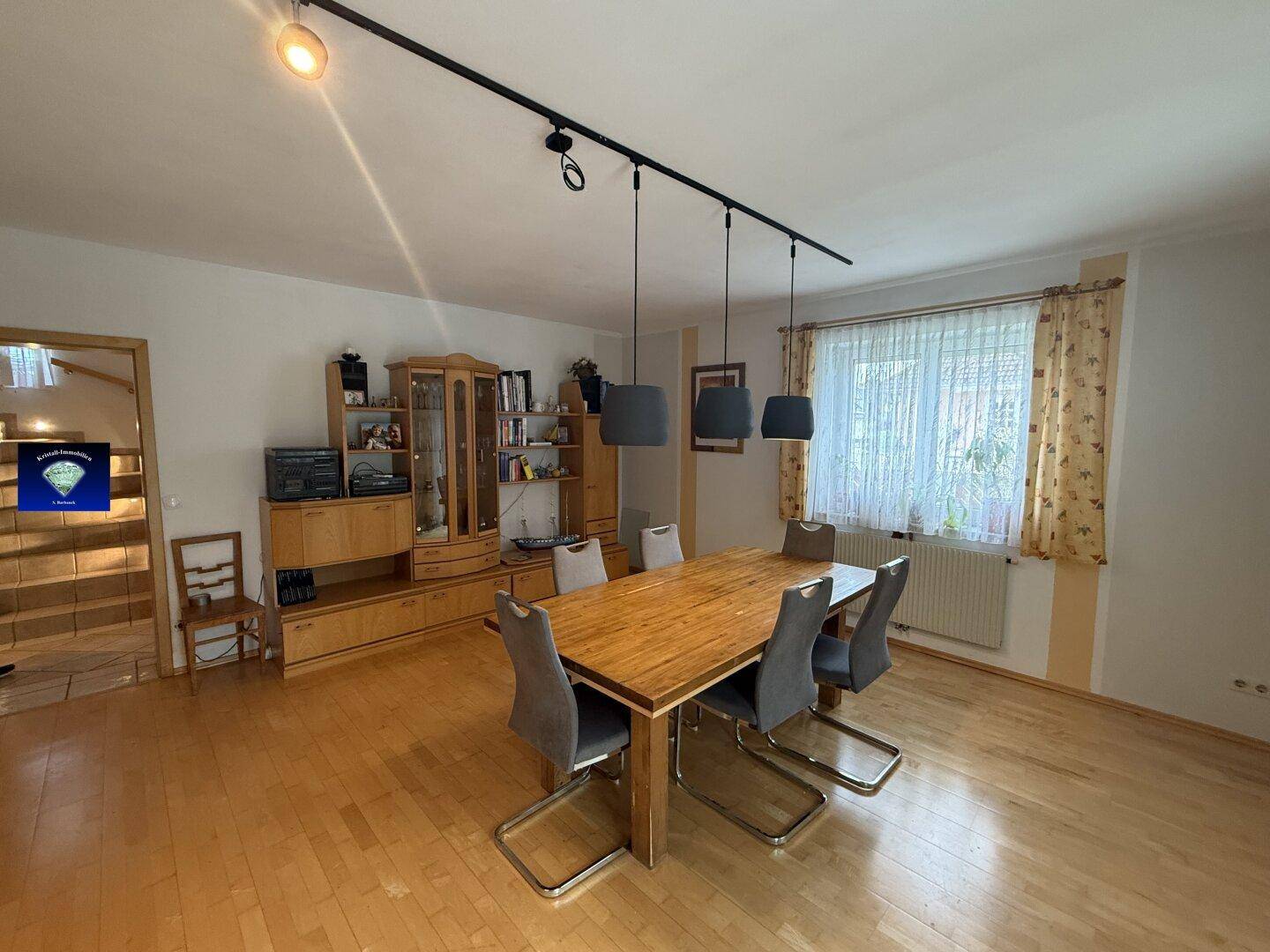 Geräumiger Wohn-Essbereich mit Holzboden, großem Esstisch und Blick auf die Treppe.