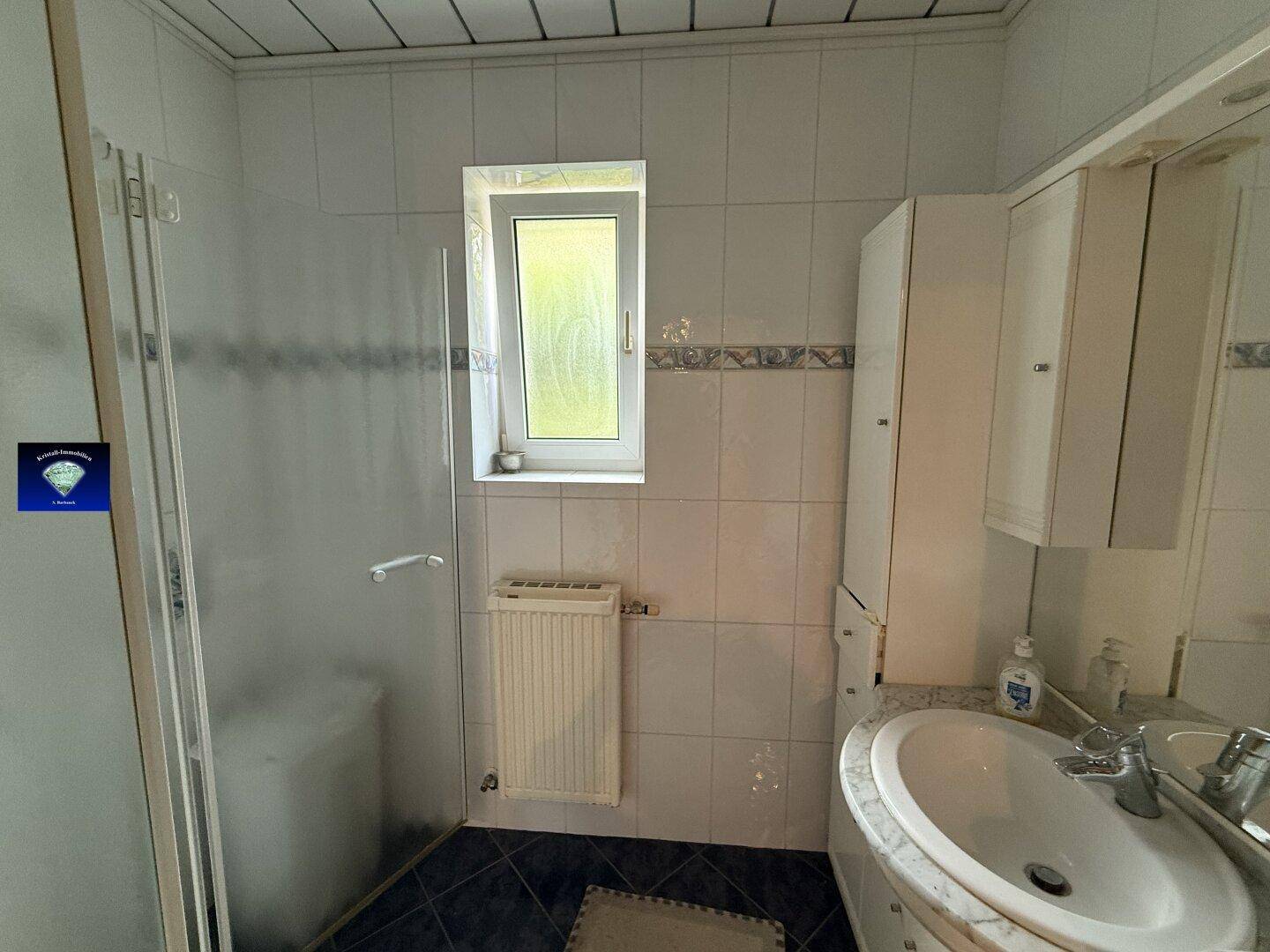 Gefliestes Badezimmer mit Dusche, Waschbecken und einem Fenster für Tageslicht.