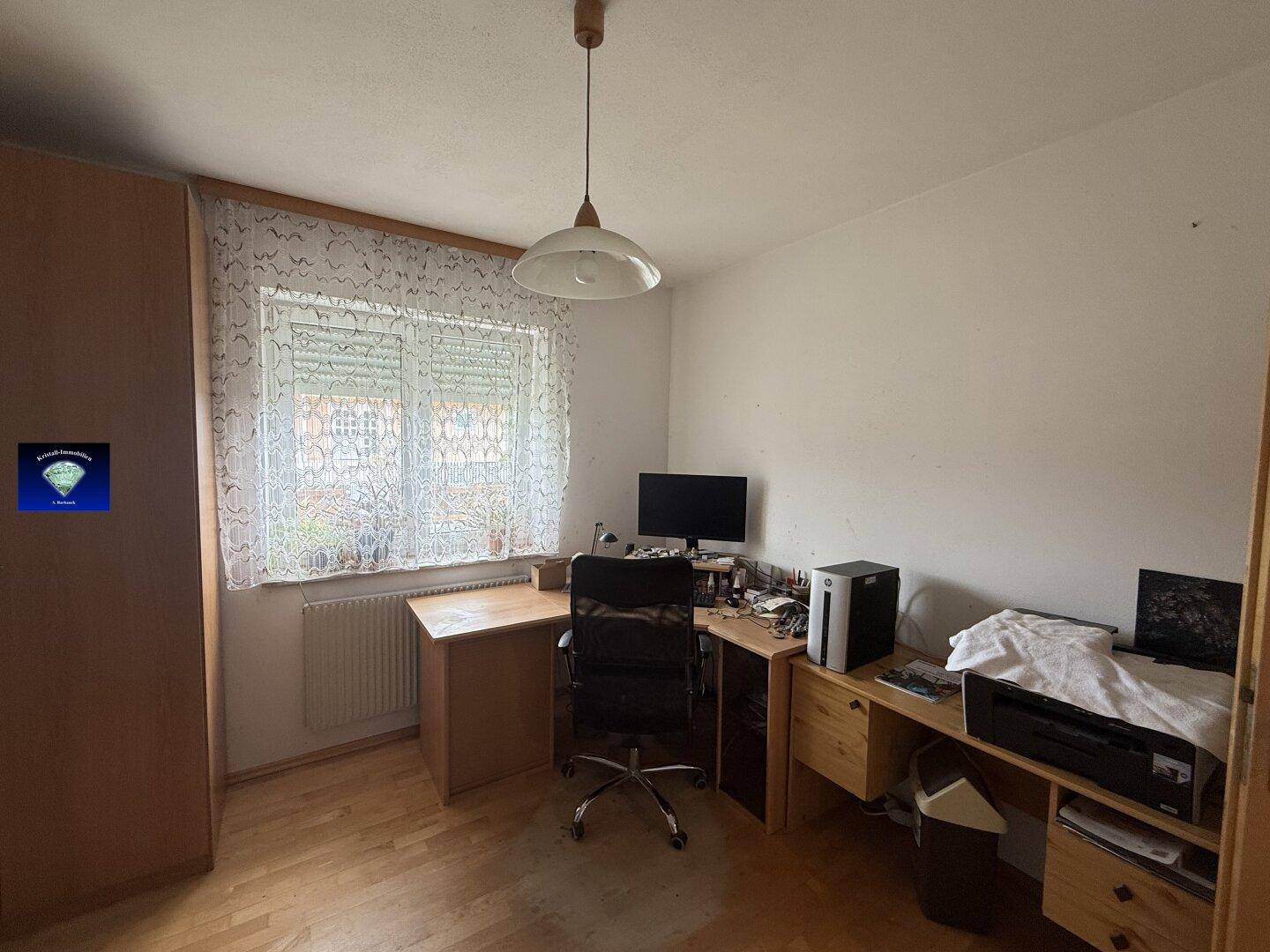Funktionales Arbeitszimmer mit Schreibtisch, Bürostuhl und Fenster für natürliche Belichtung.