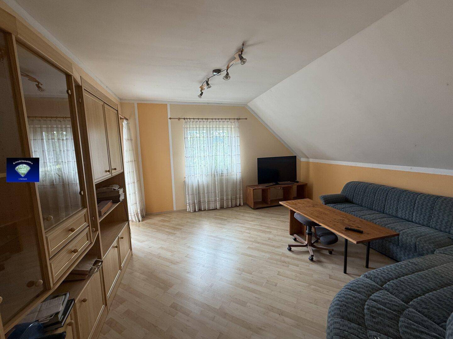 Geräumiges Wohnzimmer im Dachgeschoss mit Schrägen, Sofa und Laminatboden.
