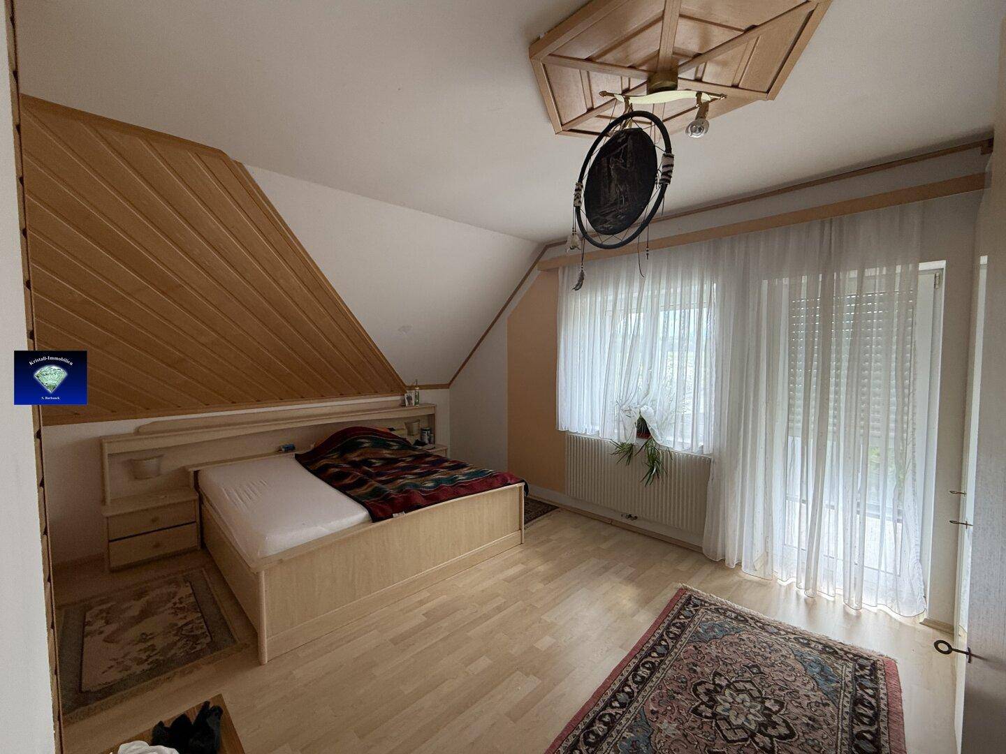 Gemütliches Schlafzimmer im Dachgeschoss mit Holzwandverkleidung, Bett und Laminatboden.