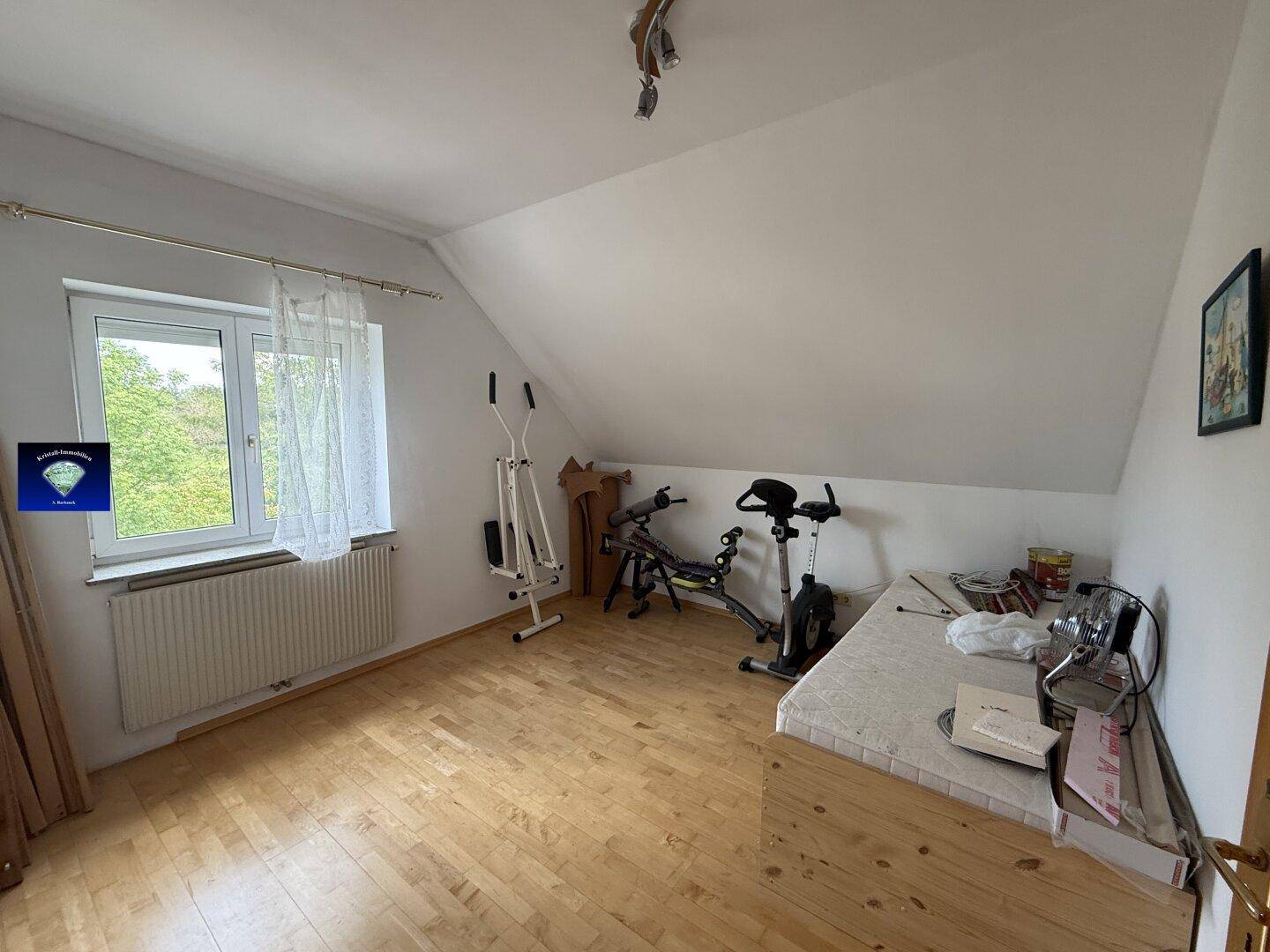 Helles Zimmer im Dachgeschoss mit Sportgeräten, Schreibtisch und Laminatboden.