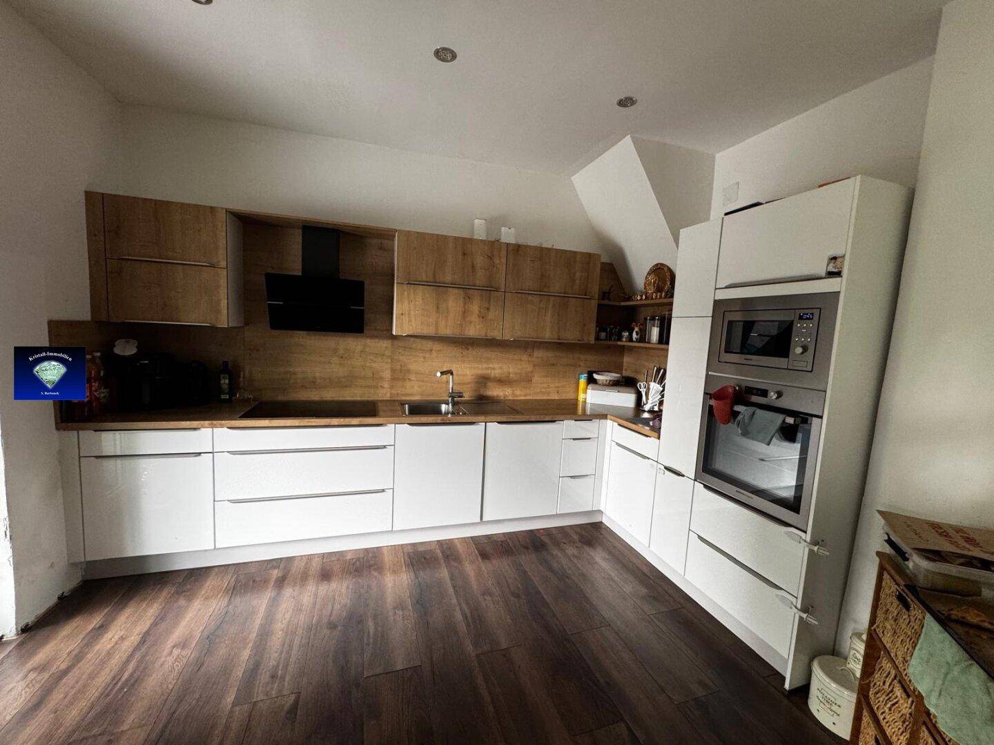 Moderne Küche mit weißen Unterschränken, Holzfronten und integrierten Geräten unter Dachschräge.