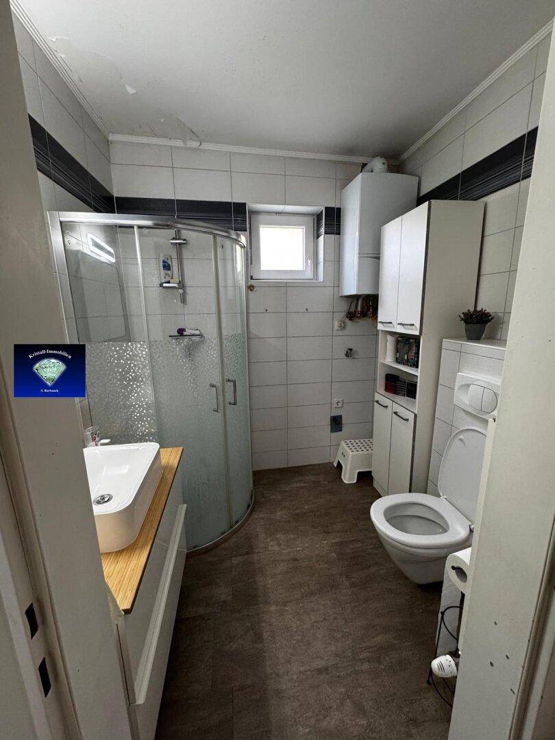 Funktionales Badezimmer mit Duschkabine, WC, Waschbecken und Fenster für Tageslicht.