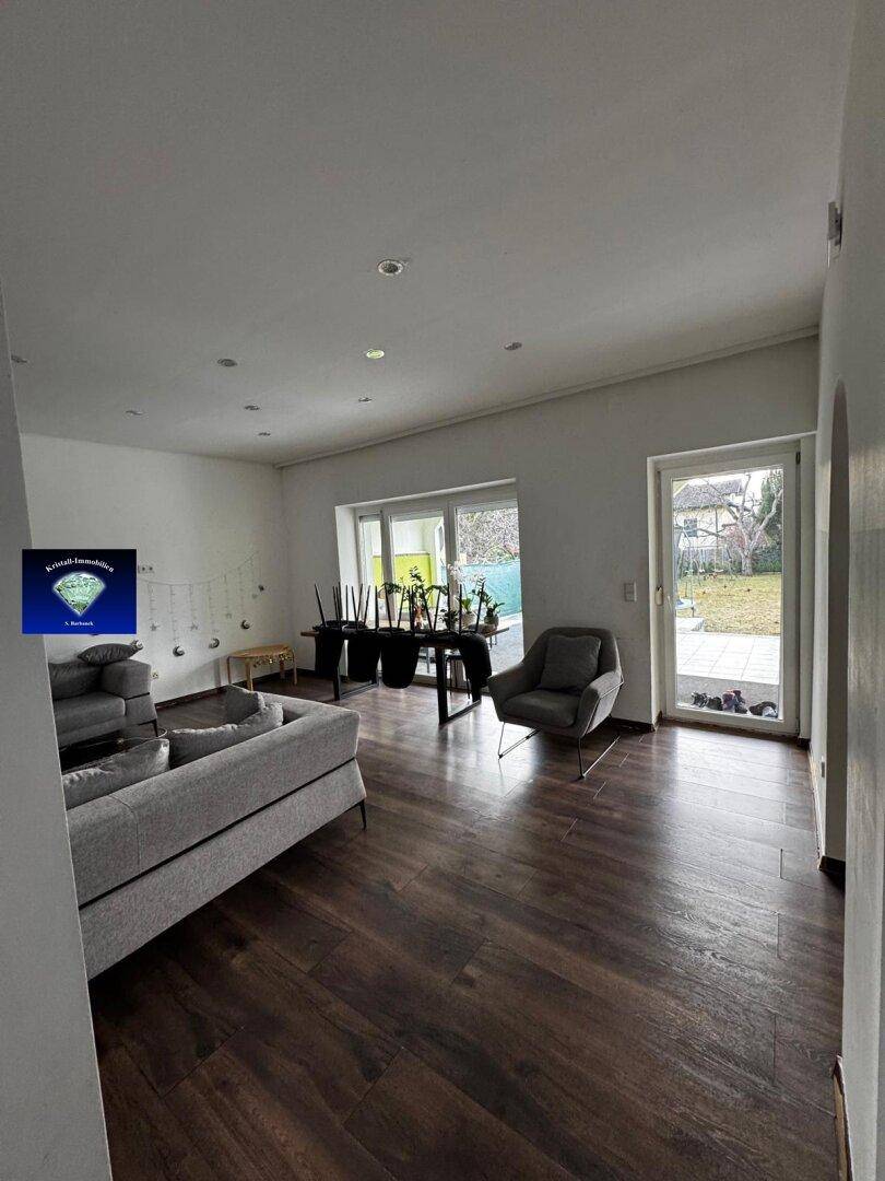 Helles Wohnzimmer mit Holzboden, großen Fenstern und direktem Zugang zum Außenbereich.
