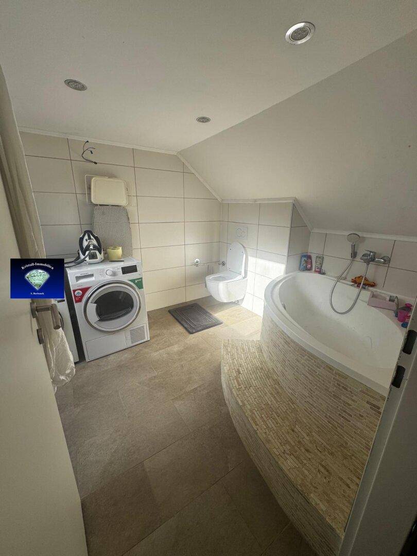 Geräumiges Badezimmer im Dachgeschoss mit Badewanne, WC und Waschmaschine unter der Schräge.