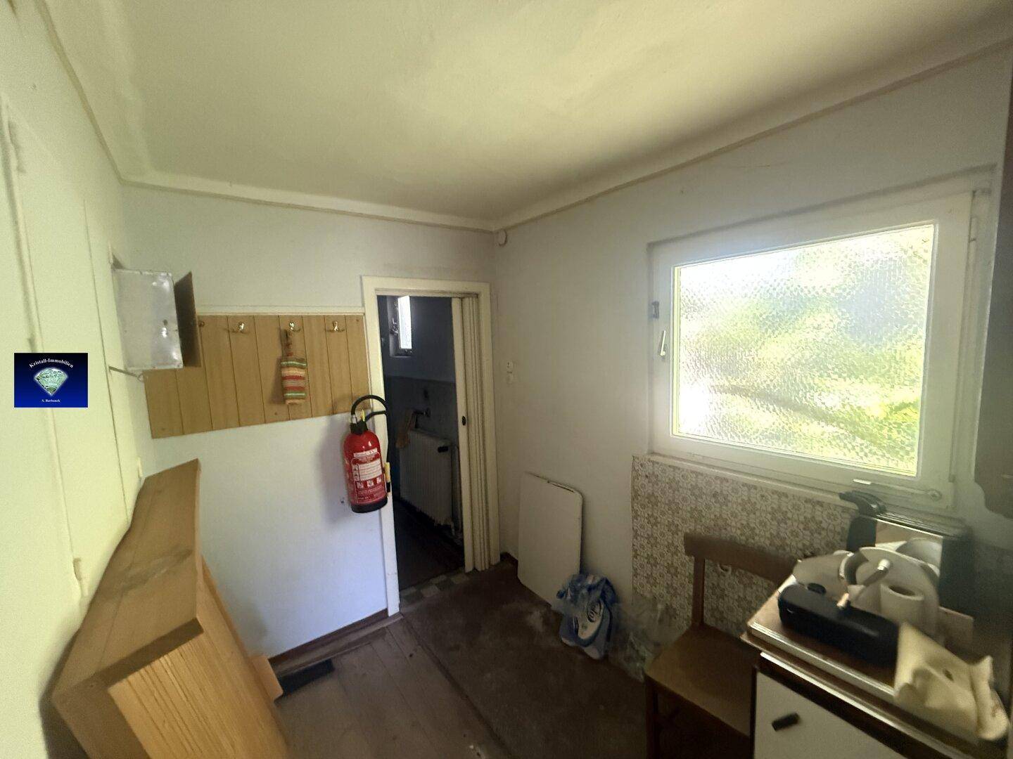 Kleiner Raum mit Fenster, Fliesenmuster an der Wand und Zugang zu einem weiteren Bereich.