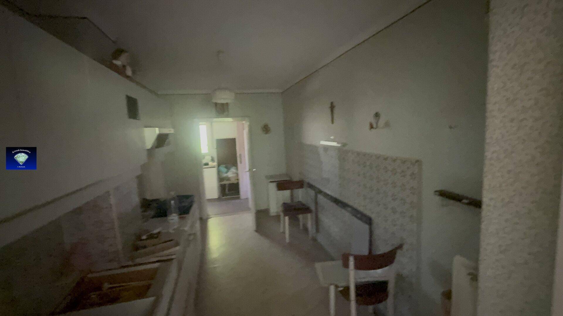 Schmale Küche mit Arbeitsplatte, Spülbecken und Fliesen an der Wand, mit Durchgang.