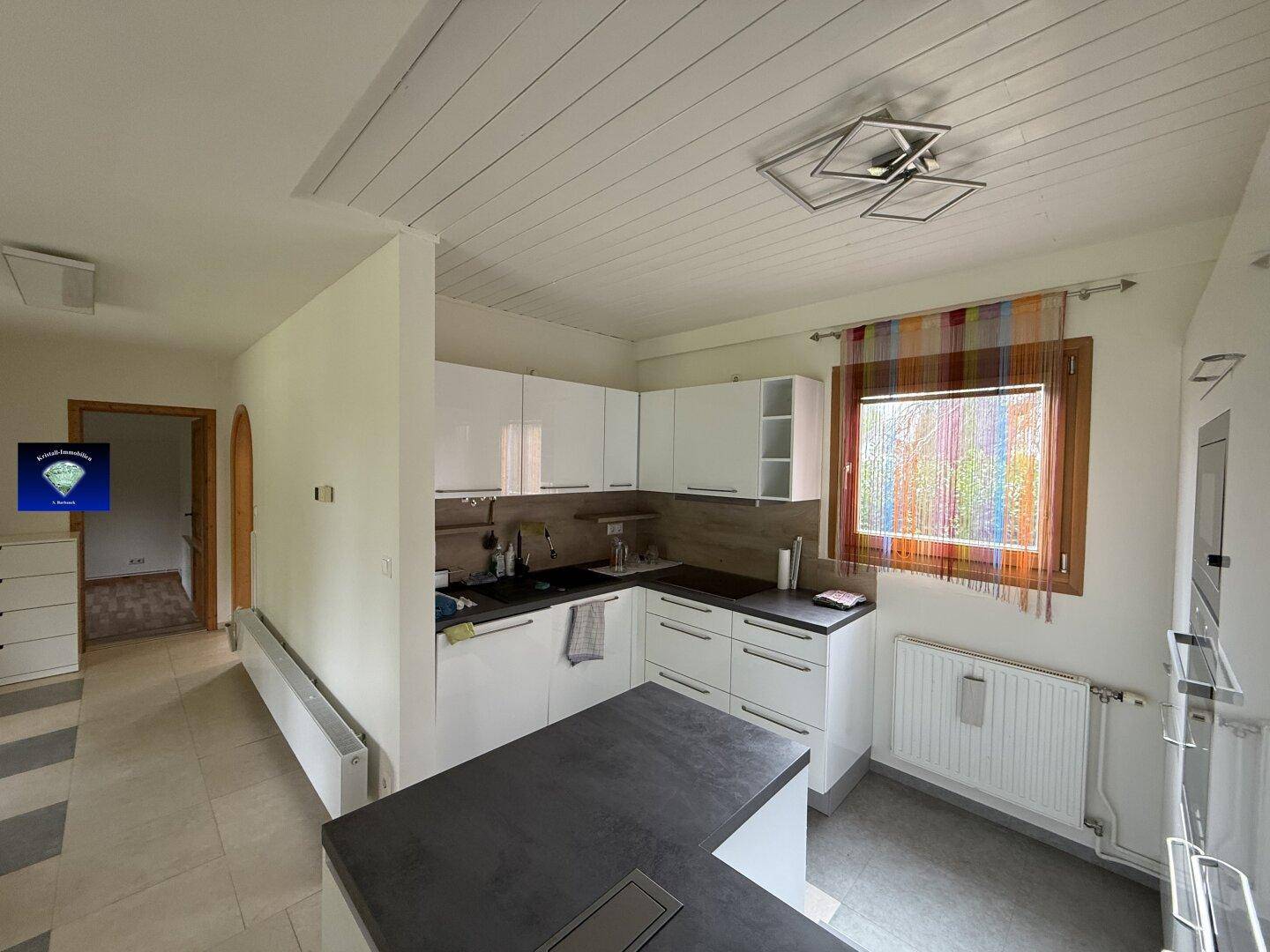 Moderne Einbauküche mit weißen Schränken und dunkler Arbeitsplatte in offenem Wohnbereich.