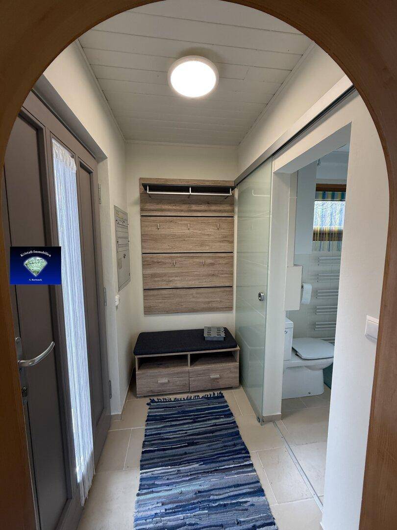 Heller Eingangsbereich mit Garderobe und Schuhbank, angrenzend an ein Badezimmer.
