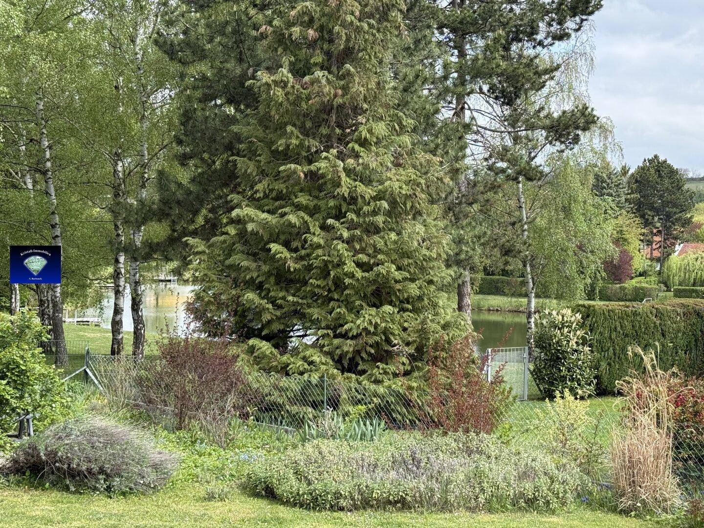 Malerischer Garten mit üppiger Vegetation und einem ruhigen See im Hintergrund.