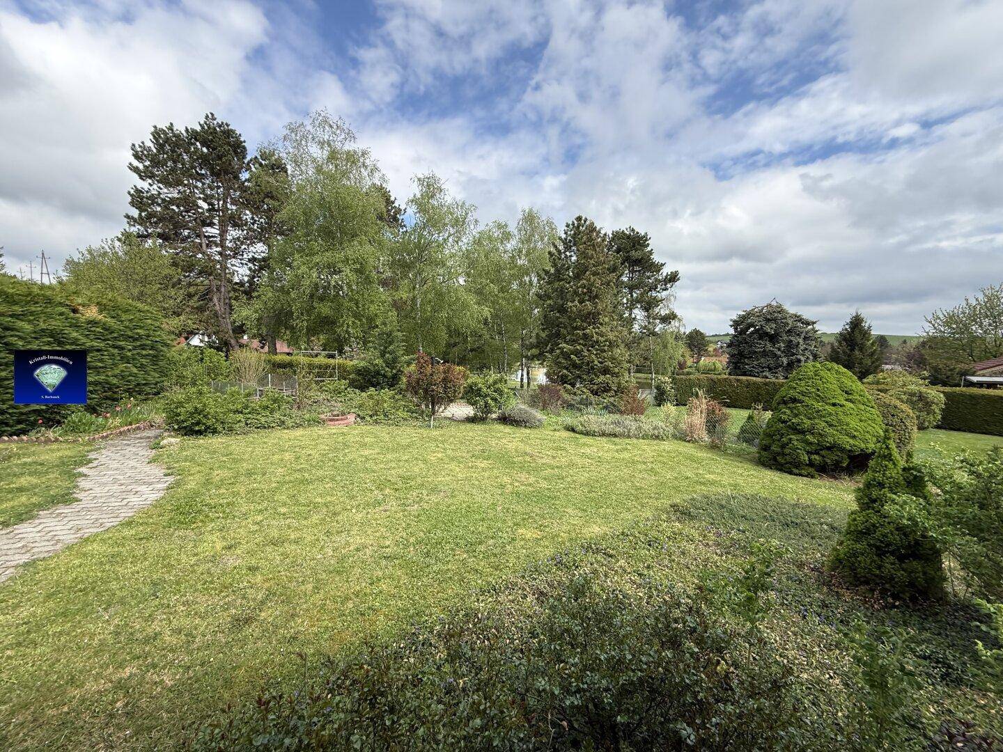 Weitläufiger, gepflegter Garten mit Rasenfläche, Bäumen und Sträuchern unter blauem Himmel.