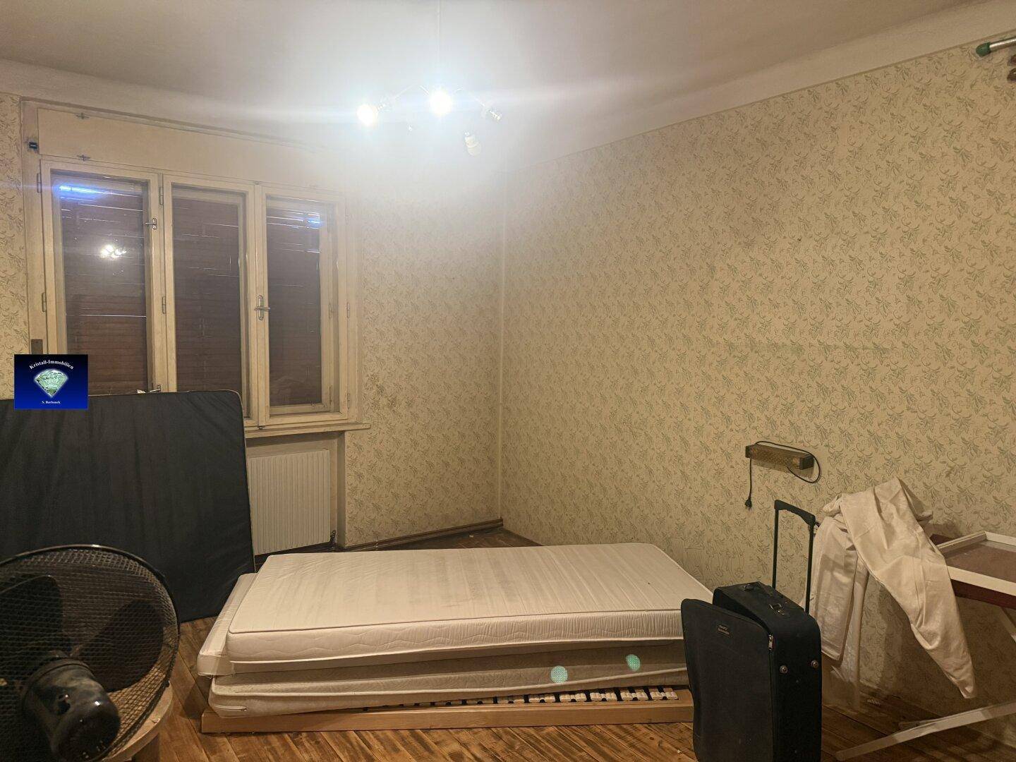 Schlafzimmer mit gemusterter Tapete, einem Bett und einem Fenster, das auf den Hof blickt.