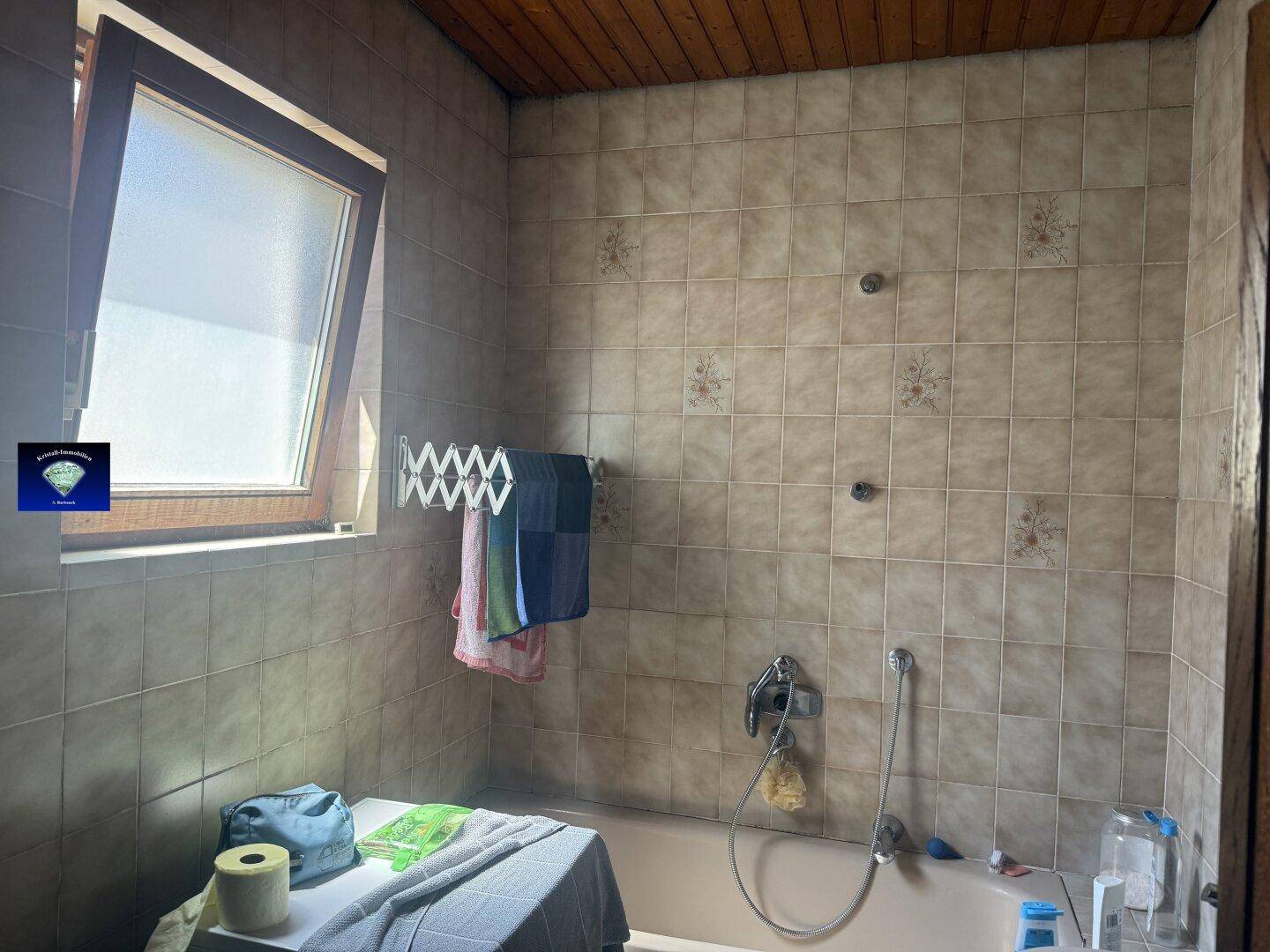Badezimmer mit beigefarbenen Fliesen, einer Badewanne und einem Dachfenster für natürliches Licht.