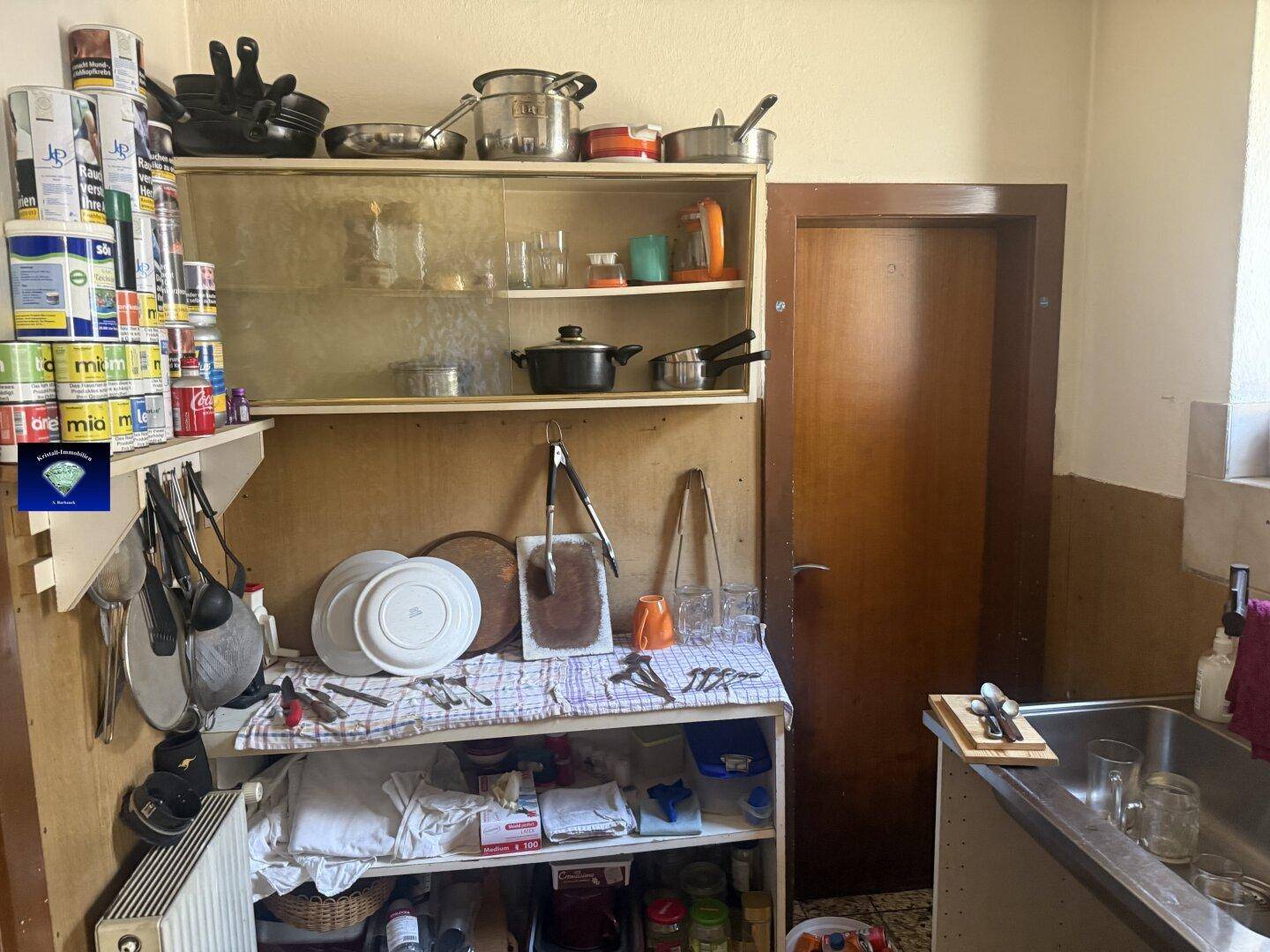 Rustikale Küche mit offenen Regalen, Geschirr und einem Spülbecken, bereit für eine Renovierung.
